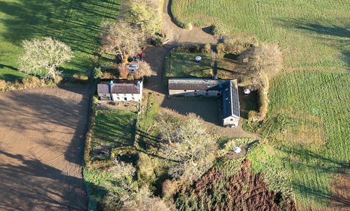 An aerial view of the Carmarthenshire house and barn during the winter, surrounded by fields and woodland